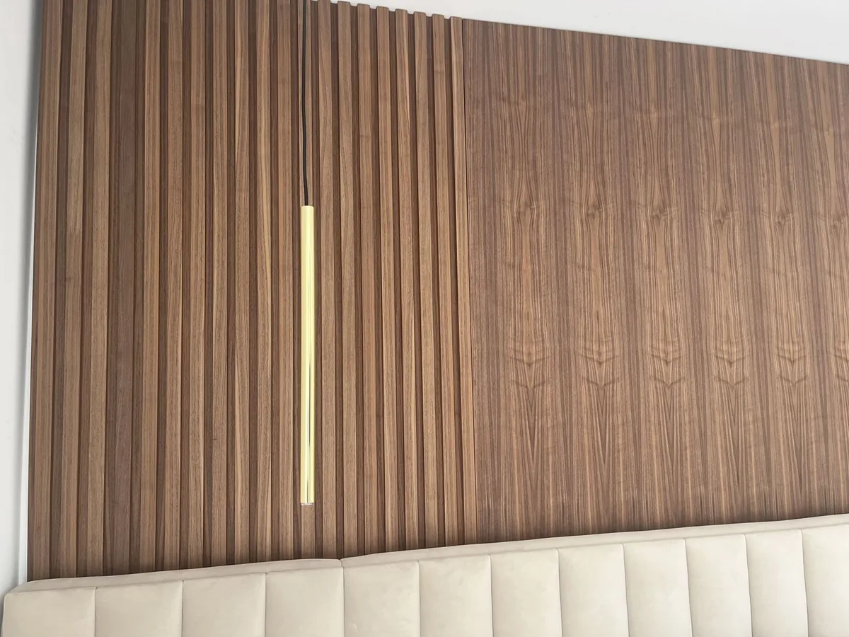 Grande plano do painel ripado em nogueira, com cabeceira estofada e suspensão em latão